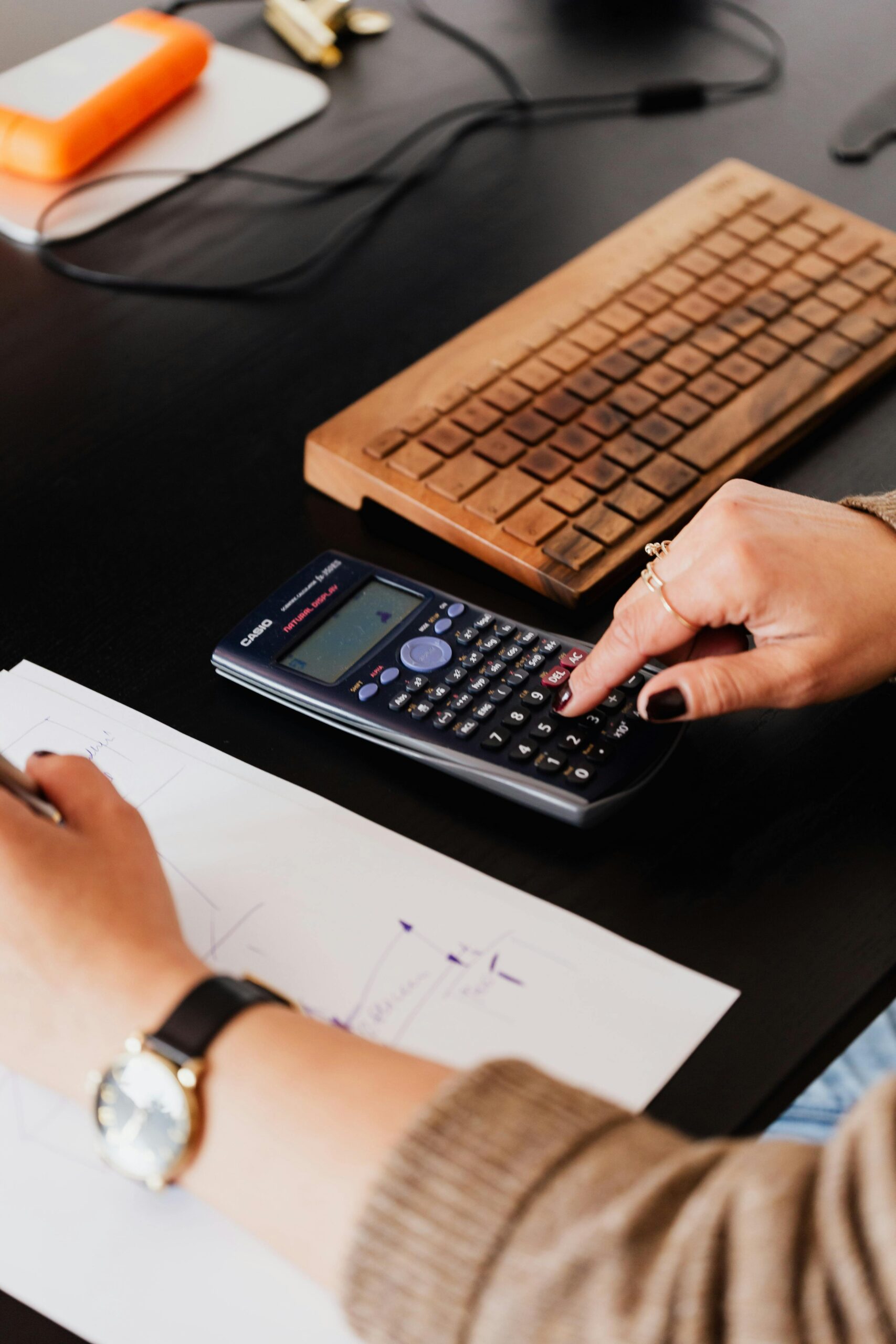 A female accountant's hands crunching numbers on a calculator and taking notes on a notepad.